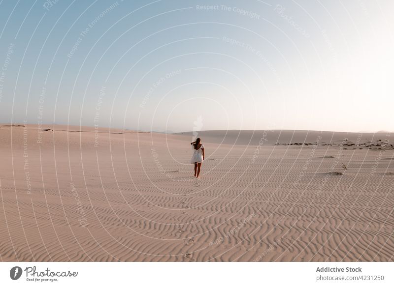 Unrecognizable traveler walking on sand in desert tourist trip vacation nature dune sky woman stroll summer tourism white dress feminine explore wanderlust