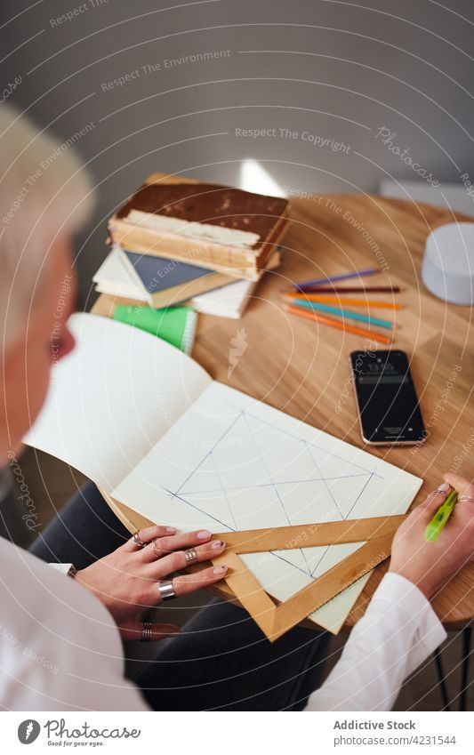 Crop astrologer drawing on paper at desk in house triangle geometry prepare astrology woman home pseudoscience divine predict future table astrologist pen