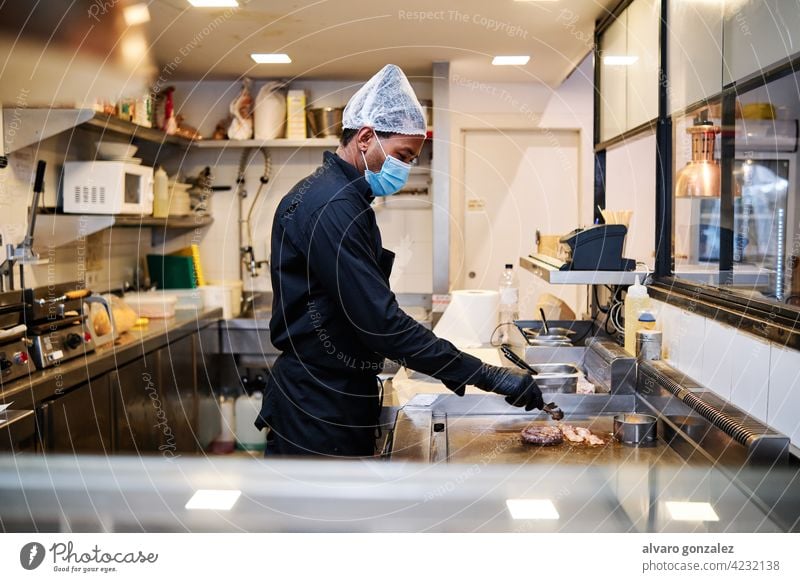 Close-up of professional latin chef man wearing a protective mask and uniform while working at restaurant kitchen. chief cooker worker staff stove indoors