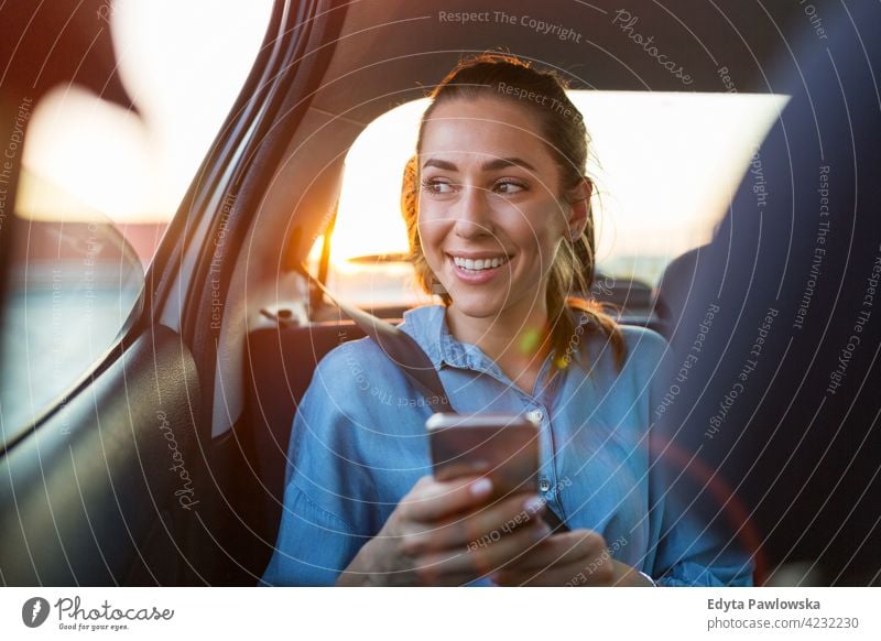 Young woman with smartphone on the back seat of a car carsharing confident smiling satisfaction female attractive beautiful young adult joy positive content