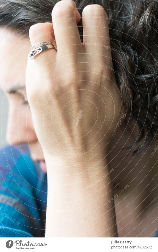 40 year old woman touching graying curly hair; female embracing natural hair color going dye free hair care grow grow out wavy quarantine silver fresh