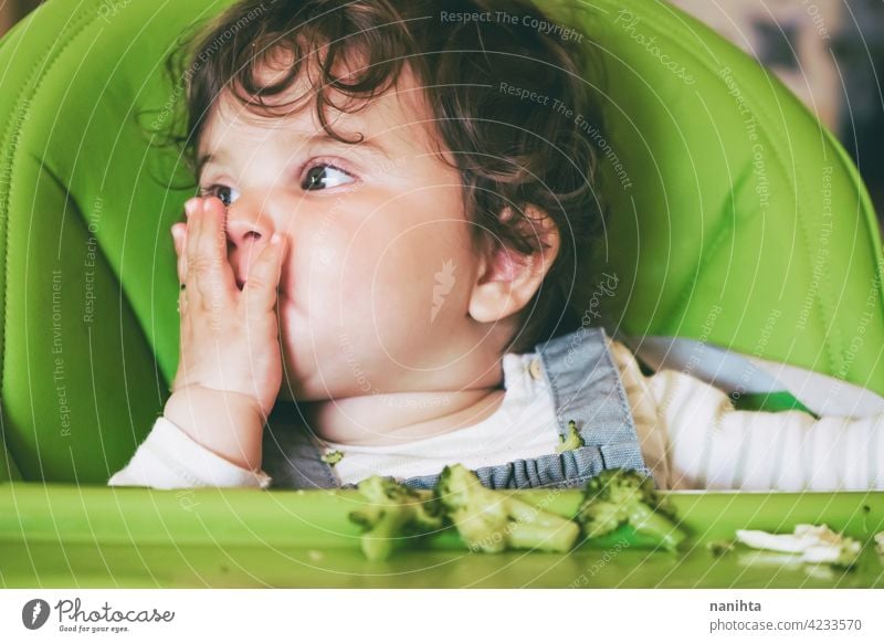 Baby eating food in her green highchair blw baby lead weading vegetables brocoli vegan vegetarian health healthy diet white caucasian complementary feeding