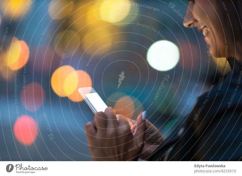 Young woman with smartphone at night in a urban city area street active people young adult casual attractive female happy Caucasian enjoying one person