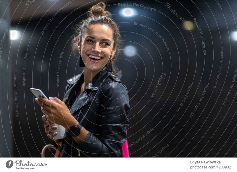 Young woman with smartphone at night in a urban city area street active people young adult casual attractive female happy Caucasian enjoying one person