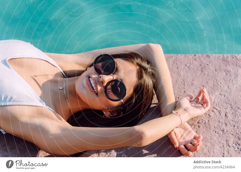 Sensual tourist in swimsuit resting against swimming pool woman lying fashion style sensual sunglasses feminine body vacation travel swimwear water ripple shiny