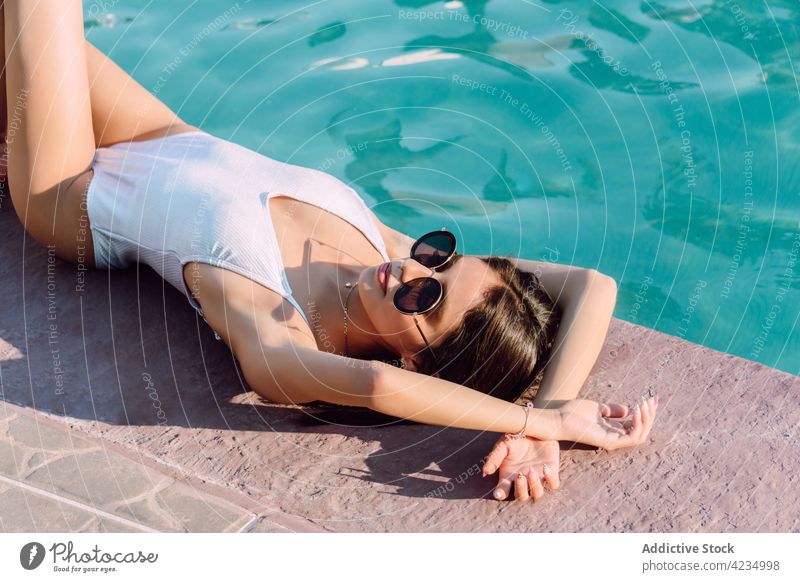 Sensual tourist in swimsuit resting against swimming pool woman lying fashion style sensual sunglasses feminine body vacation travel swimwear water ripple shiny