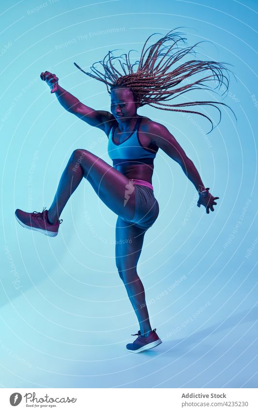 Black sportswoman with flying hair on blue background motion power afro braid muscular energy dynamic vitality sneakers modern style belly bicep muscle black