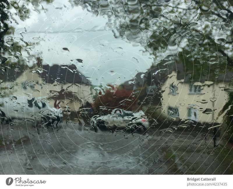 A van and a car parked on the roadside beside two white houses.Picture taken through a window and filtered by raindrops. rainy day blur stormy sky foliage