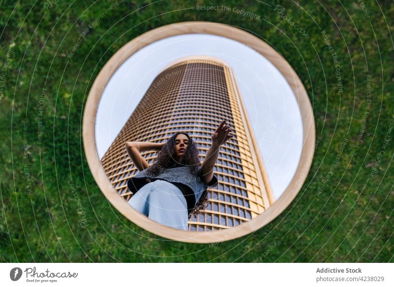 Attractive woman standing near modern skyscraper and reflecting in mirror reflection creative tower architecture style urban emotionless cool trendy calm