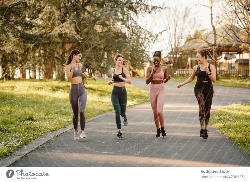 Cheerful diverse sportswomen running on footpath in urban park runner jog training cardio workout activity talk cheerful warm up exercise jogger city