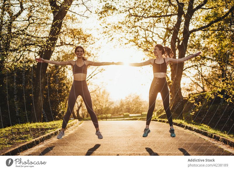 Slim female runners warming up in park at sunset sportswomen training warm up fit together athlete stretch workout fitness jump wellness exercise sportswear