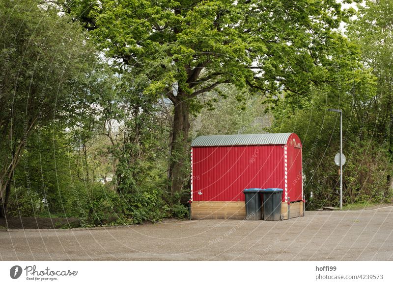 red construction trailer with waste paper bins and lots of green around it Red Site trailer Old collection ton waste bins Foliage plant trees Bushes