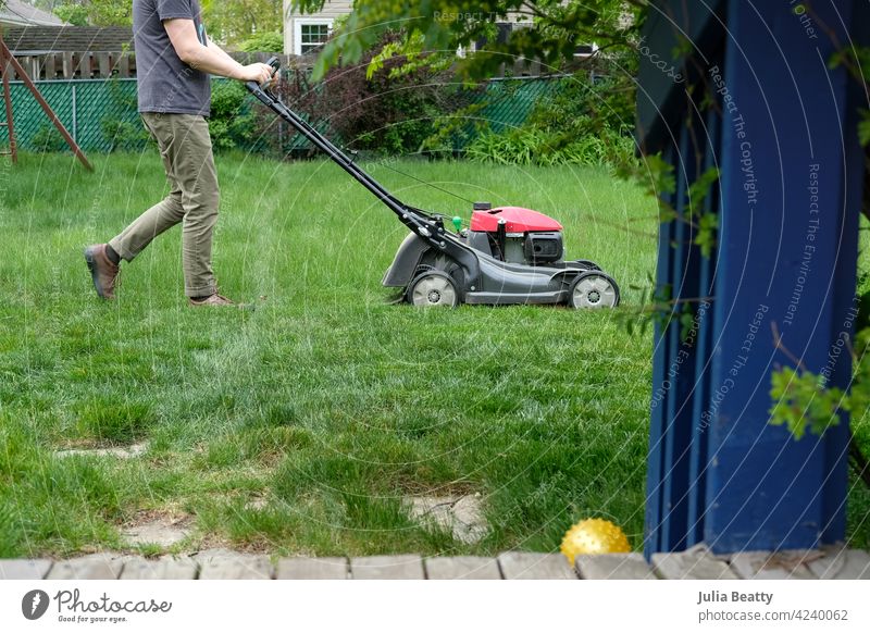 Man mowing tall grass; suburban back yard with deck and landscaping lawn mower lawnmower growth chore weekend exercise home wood garden work green gardening cut