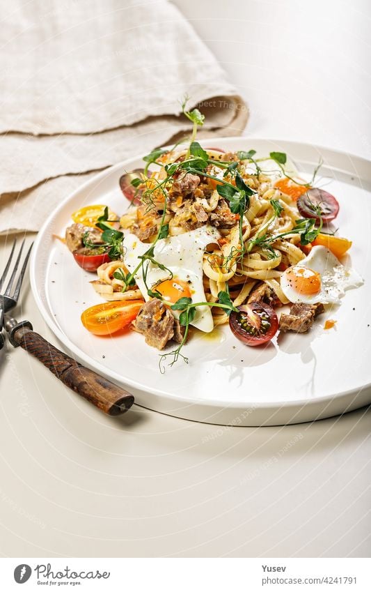 Close-up of delicious homemade spaghetti with vegetables, cheese and fried quail eggs on a round plate on a light background. Traditional Italian food. Mediterranean lunch or dinner. Copy space