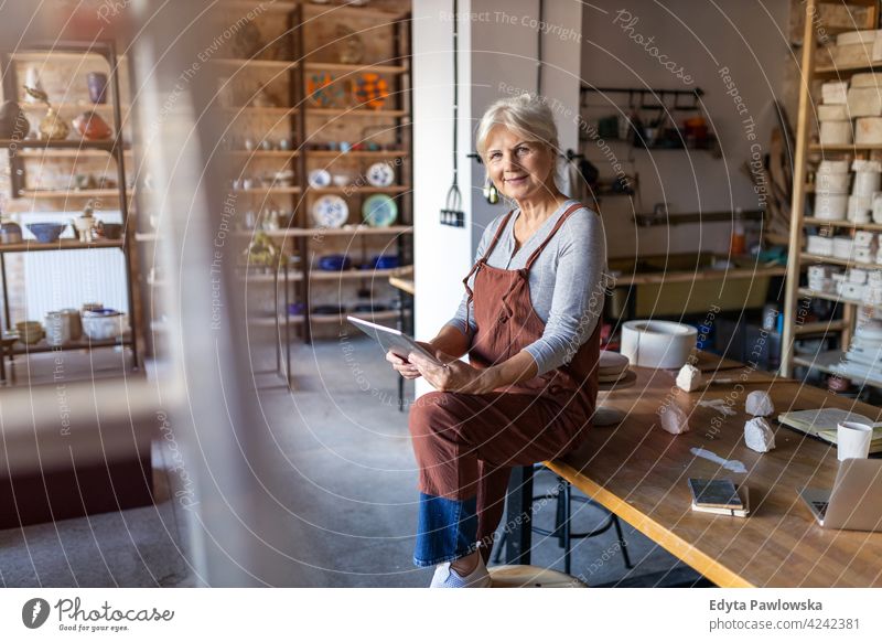 Senior craftswoman with tablet computer in art studio pottery artist ceramics work working people senior adult casual attractive female happy Caucasian enjoying