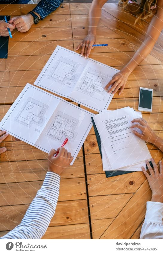 Unrecognizable architects in a work meeting looking at building plans of a house aerial architecture unrecognizable pointing teamwork brainstorming wooden table