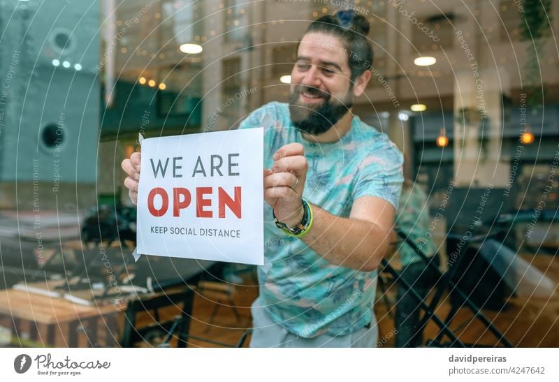 Man placing opening poster after coronavirus man notice covid-19 coffee shop happy excited hopeful smiling sticking poster we are open quarantine reopening bar