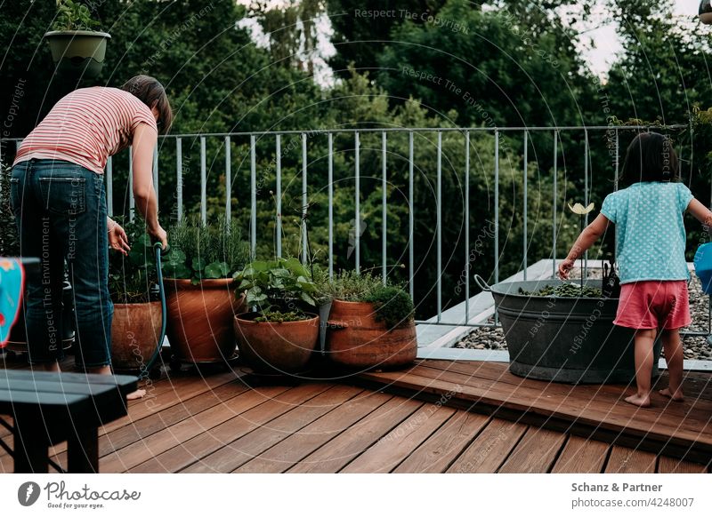 Mom and daughter watering the flowers on the balcony Balcony flower watering Mother Daughter Child Family out Terrace flower tub Cast family life Woman Parents