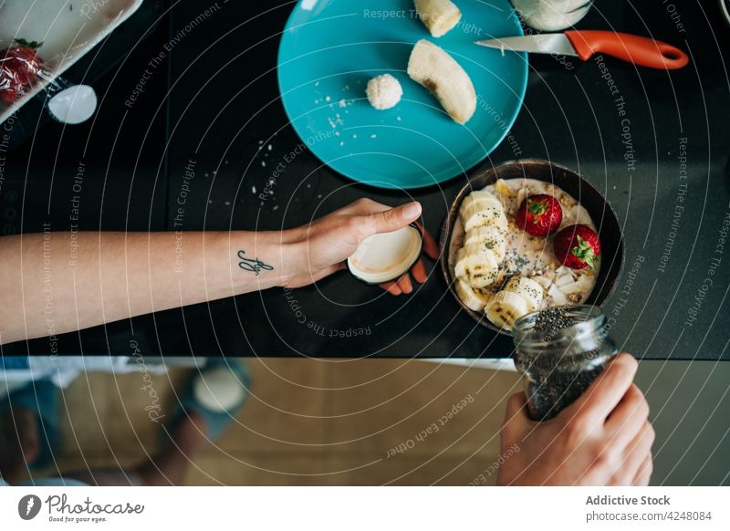 Crop faceless person garnishing delicious oatmeal with black sesame porridge topping healthy food banana strawberry kitchen breakfast tasty fresh organic yummy