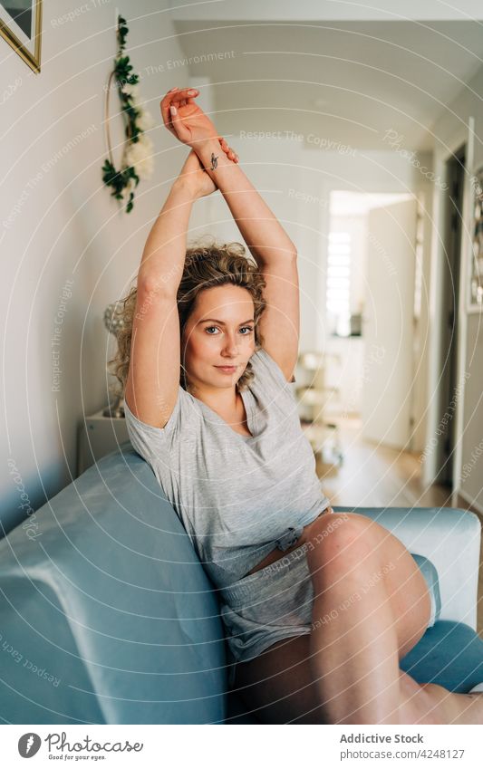 Young woman sitting on sofa positive content living room cozy comfort rest couch attractive young lifestyle beautiful slim glad stretching appearance satisfied