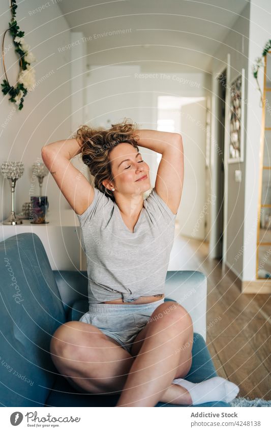 Young woman sitting on sofa positive content living room cozy comfort rest couch attractive young lifestyle eyes closed beautiful slim glad stretching