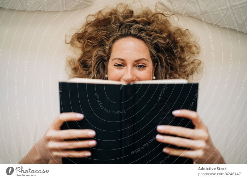 Woman reading book while lying on bed woman rest home happy comfort bookworm lazy weekend relax delight female young curly hair morning chill bedroom cozy calm