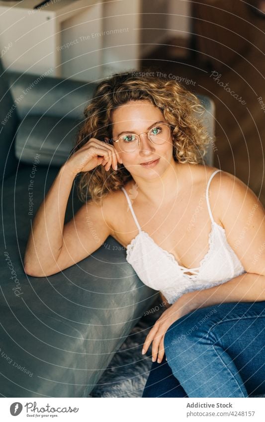 Smiling young woman leaning on couch sitting on floor at home relax smile positive style confident happy cozy apartment comfort content female curly hair blond