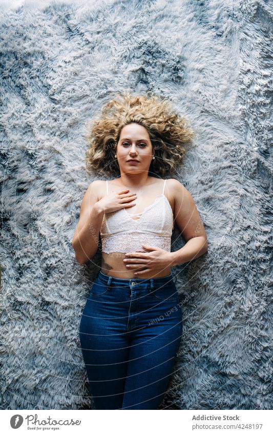 Relaxed young woman lying on carpet rest calm tranquil home serene chill feminine comfort appearance female blond curly hair bra jeans body allure cozy