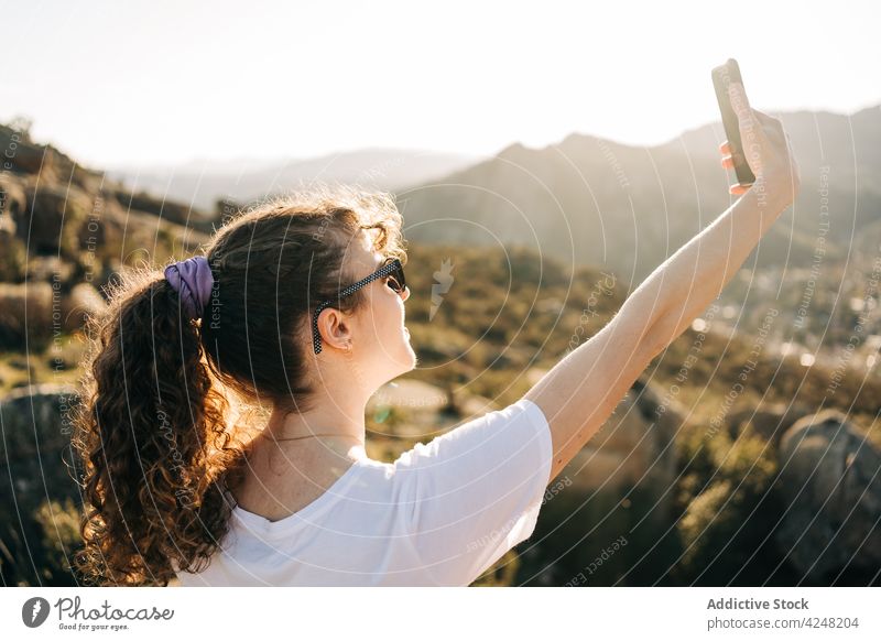 Content young lady taking selfie during vacation in mountains woman traveler journey take photo happy tourism smartphone female casual sunglasses sunlight