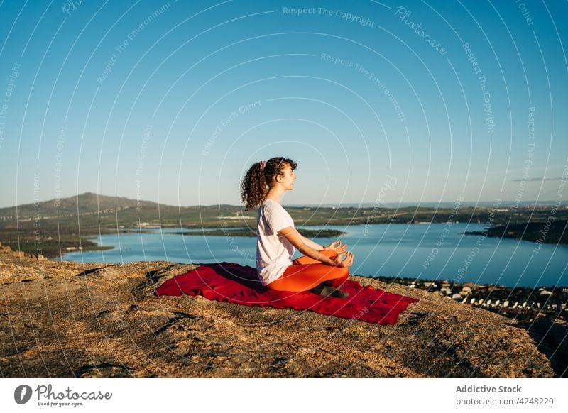 Young female traveler recreating in Padmasana yoga pose on rocky hill woman padmasana lotus pose meditate eyes closed harmony recreation nature calm peaceful