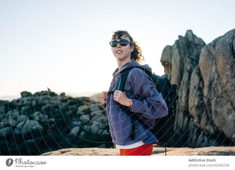 Positive young female hiker smiling and enjoying mountain views woman traveler smile explore journey trip trekking nature valley happy curly hair hoodie