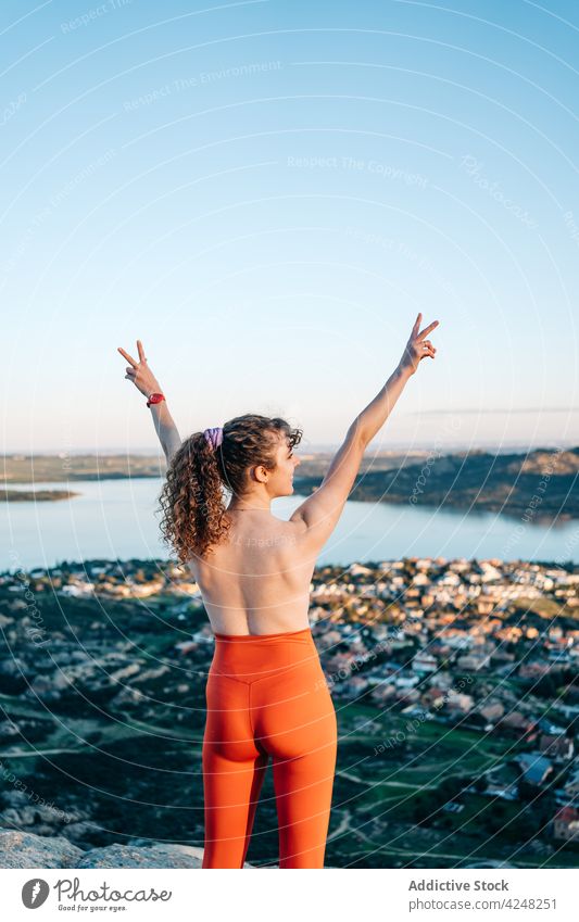 Fit topless woman showing V sign with raised arms on rocky mountain v sign happy traveler smile joy content positive town tourist enjoy female young curly hair