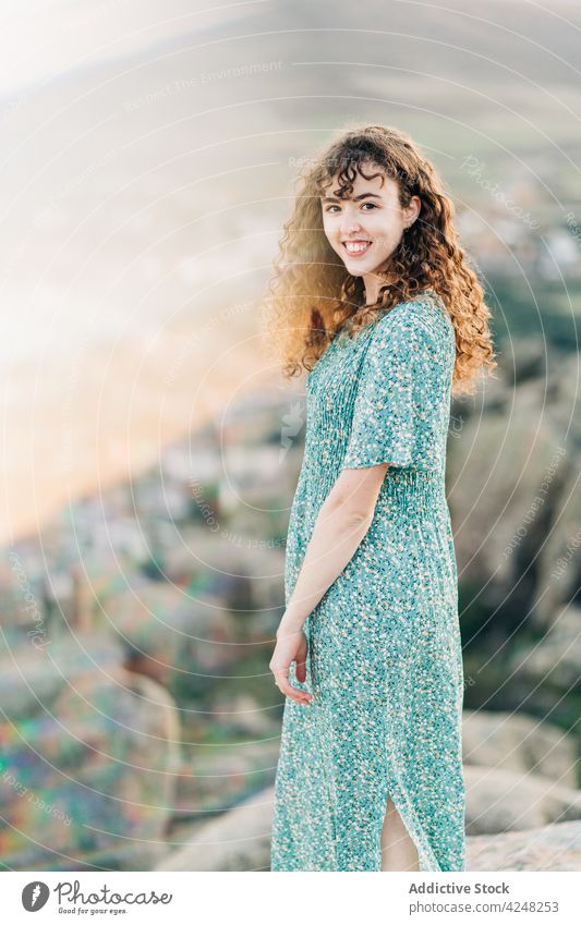 Smiling barefoot woman in sundress standing on rocky hill cheerful highland nature toothy smile carefree attractive content positive young mountain summer stone