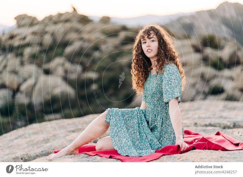 Attractive woman resting on plaid in highlands nature hilltop sundress positive mountain rocky barefoot attractive content young summer stone glad outfit maxi