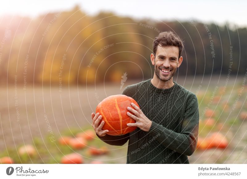 Man holding pumpkin in pumpkin patch field halloween nature park autumn fall man adult young male people happy smiling fun caucasian enjoying outdoors