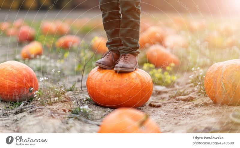 Boy standing on pumpkin in pumpkin patch legs boots shoes no face halloween nature field park autumn fall family boy kids children people fun joy outdoors