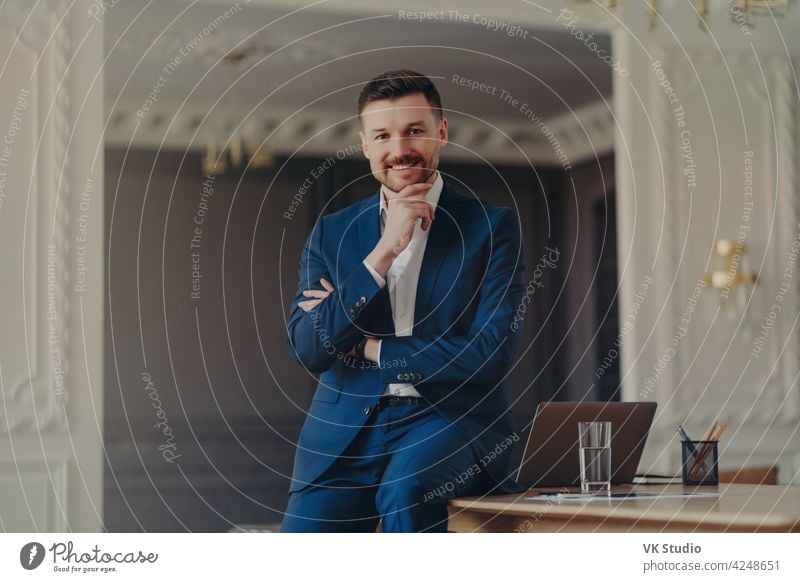 Portrait of smiling confident businessman sitting on office desk laptop handsome looking happy positive young successful modern organized professional work