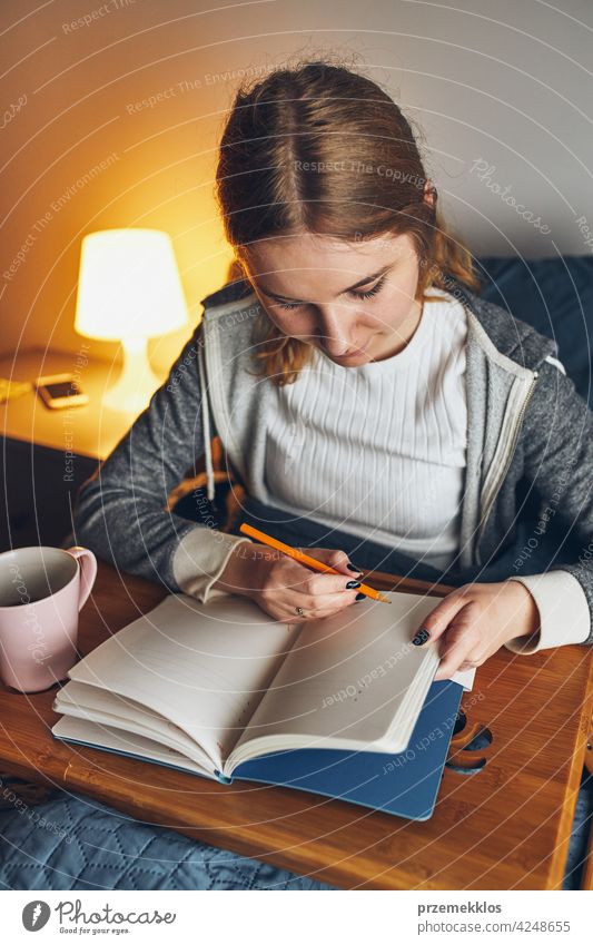 Student learning at home. Young woman making notes, reading and learning from notepad. Girl writing journal sitting in bed education indoor student working