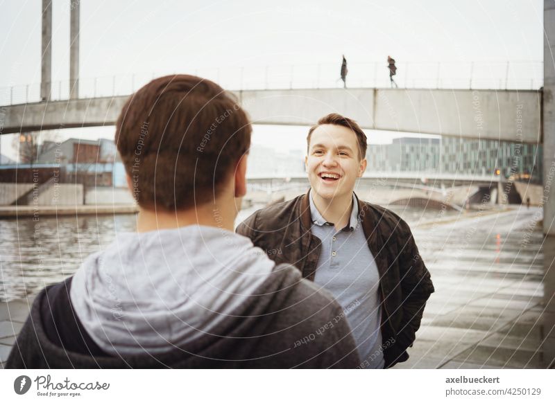 two male teenage friends having a fun conversation by the river candid laughing talking authentic lifestyle real people outside man men smiling friendship young