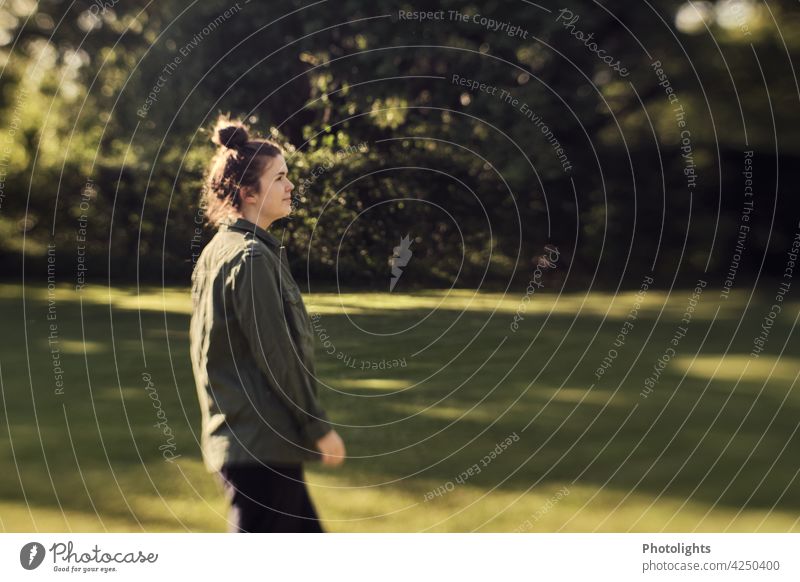 Young woman walking in a park To go for a walk Tree Forest Lawn Grass trees Meadow Nature Exterior shot Green Environment side view Braids pinned up Park Garden