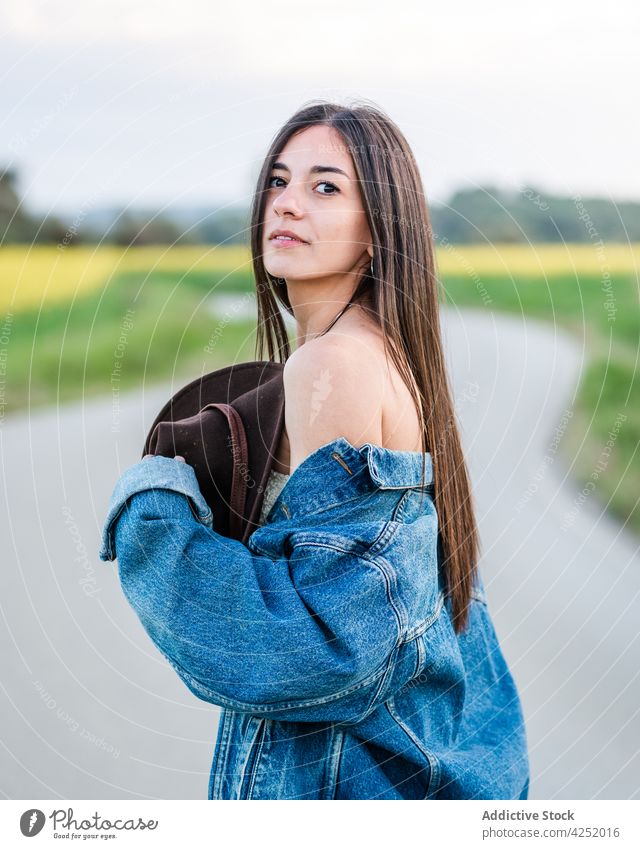 Attractive woman standing on rural roadway peaceful countryside nature serene dreamy bare shoulders appearance content field young feminine casual positive