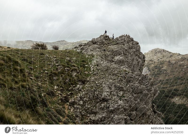 Distant hikers standing on rough mountain plateau highland summit terrain admire cloudy wanderlust altitude formation nature traveler trekking rock adventure