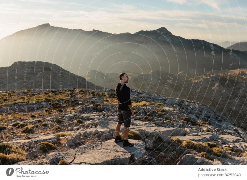 Unrecognizable man resting on rough mountain peak hiker highland sunset admire nature traveler trekking stand thoughtful sundown rock adventure seville male