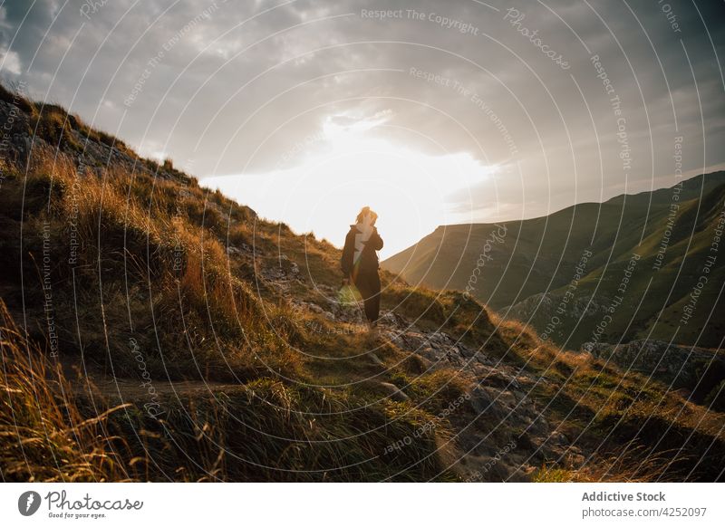 Hiking woman on slope of mountain in sunset hike downhill walk valley backpack highland explore traveler grass wanderlust sky landscape adventure tourism cloudy