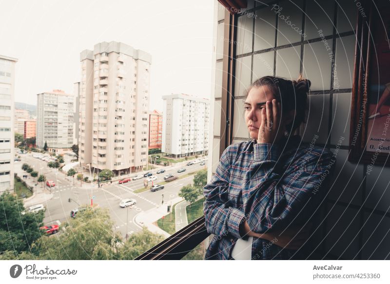 Worried woman looking from the window of her flat, mental health concept in the city, depression with copy space anxiety frustration problem sad sadness