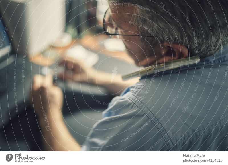 A senior man sitting at a desk in front of a laptop computer business technology crypto trade finance person block chain chart shopping book internet office