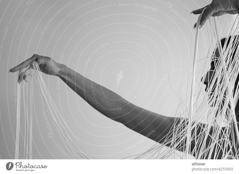 black and white Image of the profile of a young attractive woman with uncovered shoulders, who decoratively draws the white threads of a string curtain with her hands, copy space