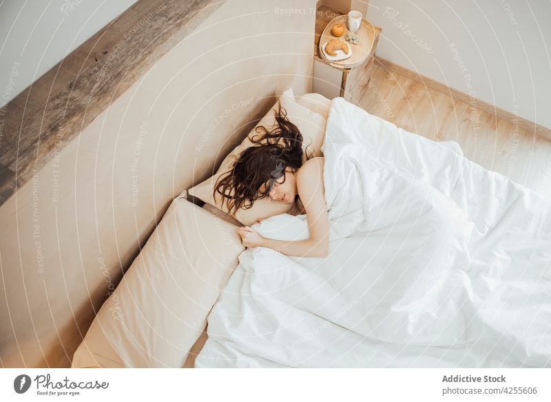 Young woman sleeping peacefully on cozy bed in morning comfort relax dream bed time asleep bedroom lying duvet lazy pillow nap eyes closed blanket at home