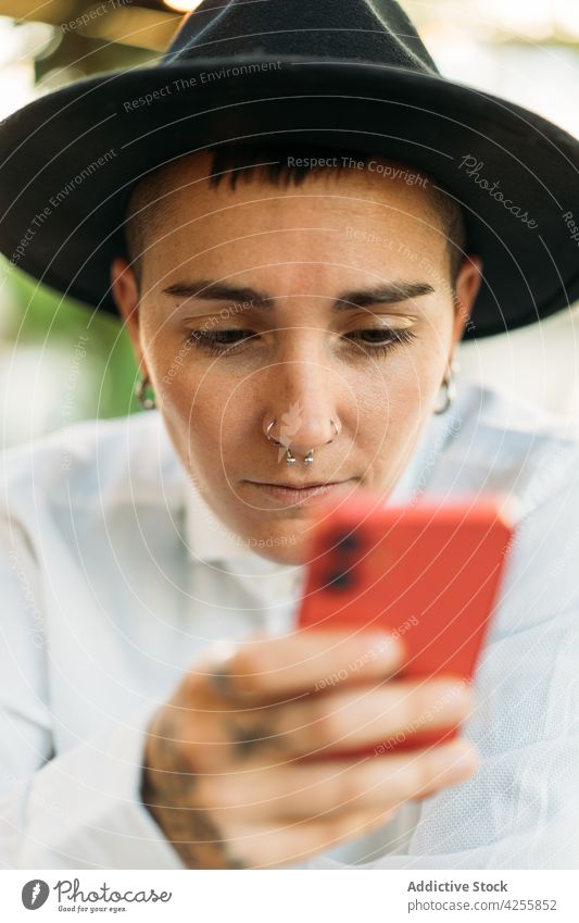 Pensive tomboy with smartphone in cafe woman transgender eccentric identity queer style agender serious device think white shirt weird unique accessory accept