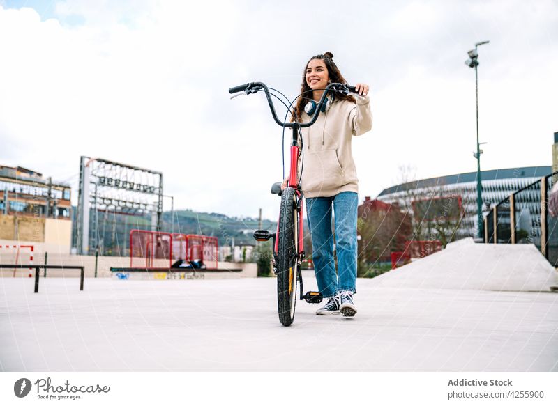 Positive woman riding bicycle in urban park positive smile cheerful ride city activity happy female hoodie jeans hobby active modern denim contemporary leisure